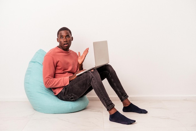 Joven afroamericano sentado en una bocanada usando una laptop aislada de fondo blanco sorprendido y conmocionado