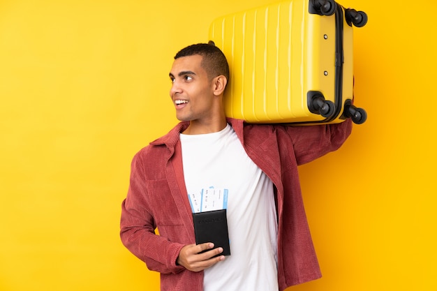 Foto joven afroamericano sobre pared amarilla aislada en vacaciones con maleta y pasaporte