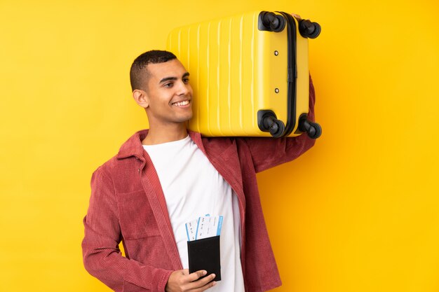 Foto joven afroamericano sobre pared amarilla aislada en vacaciones con maleta y pasaporte