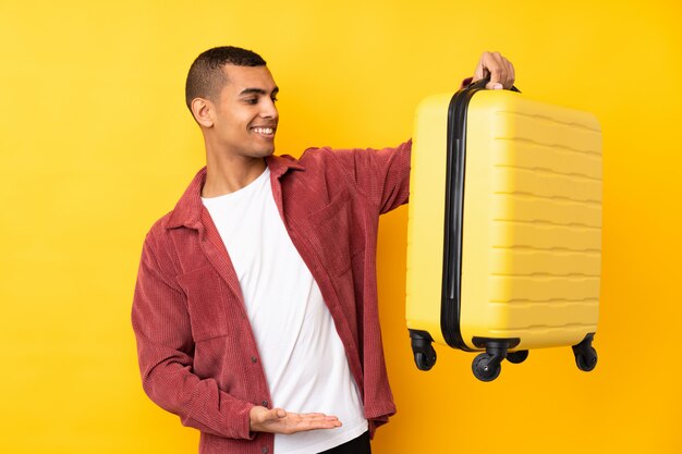 Foto joven afroamericano sobre pared amarilla aislada en vacaciones con maleta de viaje