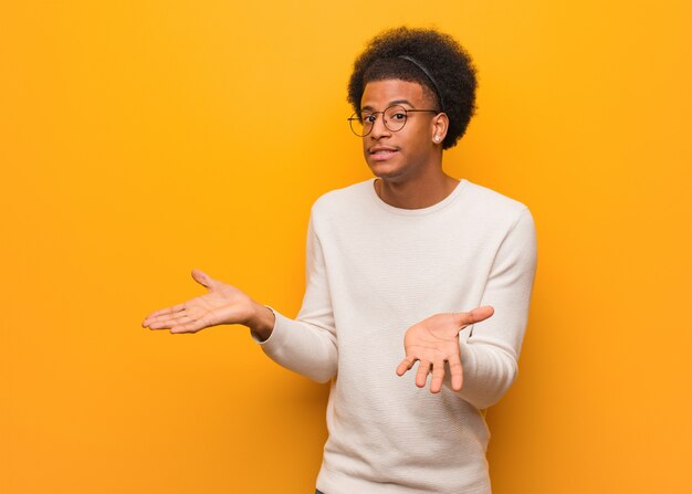 Joven afroamericano sobre una pared naranja confundido y dudoso