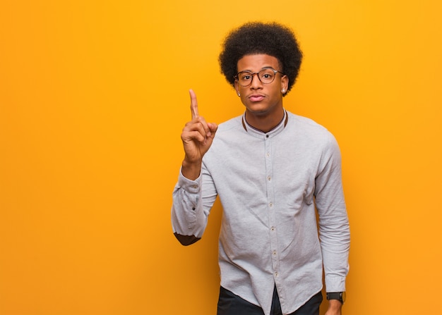 Joven afroamericano sobre una pared naranja con una idea, concepto de inspiración