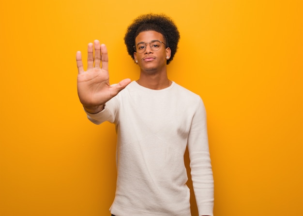 Joven afroamericano sobre una pared naranja poniendo la mano delante