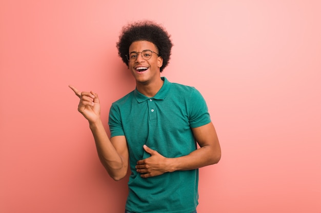 Joven afroamericano sobre una pared rosa apuntando hacia el lado con el dedo