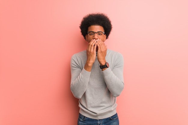 Joven afroamericano sobre una pared rosa muy asustada y asustada escondida