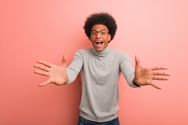 Joven afroamericano sobre una pared rosa muy feliz dando un abrazo al frente