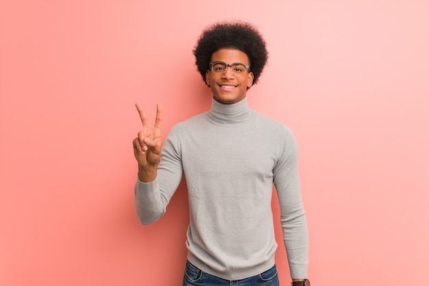 Joven afroamericano sobre una pared rosa que muestra el número dos