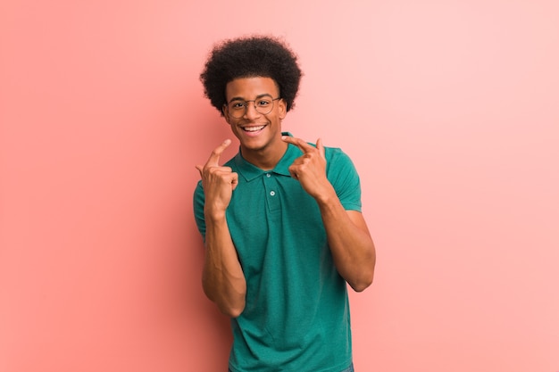 Joven afroamericano sobre una pared rosa sonríe, apuntando la boca