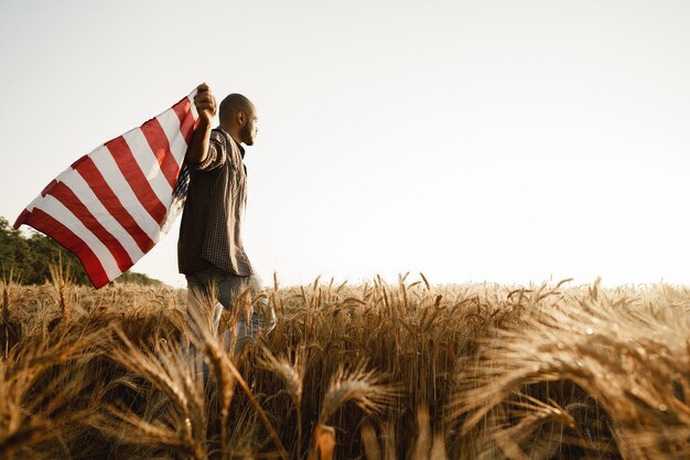 Joven afroamericano sosteniendo la bandera nacional de Estados Unidos a través del campo de trigo