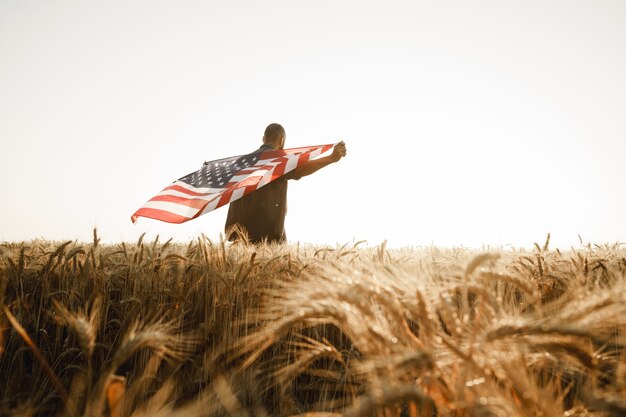 Joven afroamericano sosteniendo la bandera nacional de Estados Unidos a través del campo de trigo