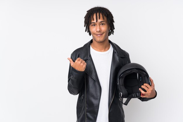 Joven afroamericano sosteniendo un casco de moto aislado en blanco apuntando hacia un lado para presentar un producto