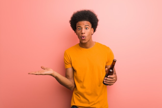 Joven afroamericano sosteniendo una cerveza sosteniendo algo en la mano de la palma