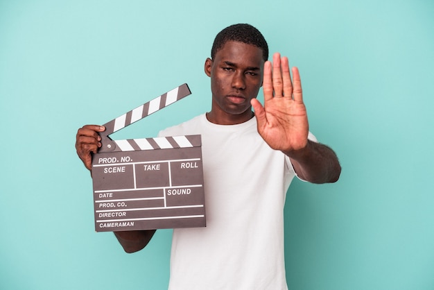 Joven afroamericano sosteniendo claqueta aislado sobre fondo azul de pie con la mano extendida mostrando la señal de stop, impidiéndote.