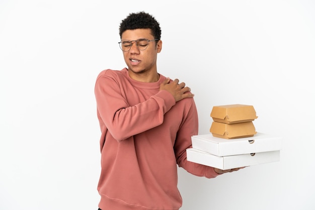 Joven afroamericano sosteniendo una hamburguesa y pizzas aislado sobre fondo blanco que sufre de dolor en el hombro por haber hecho un esfuerzo