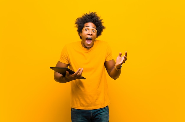 Joven afroamericano con una tableta contra backgrou naranja