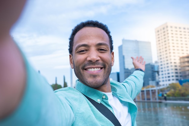 Joven afroamericano tomándose un selfie sonriendo feliz mostrando la nueva ciudad donde vive