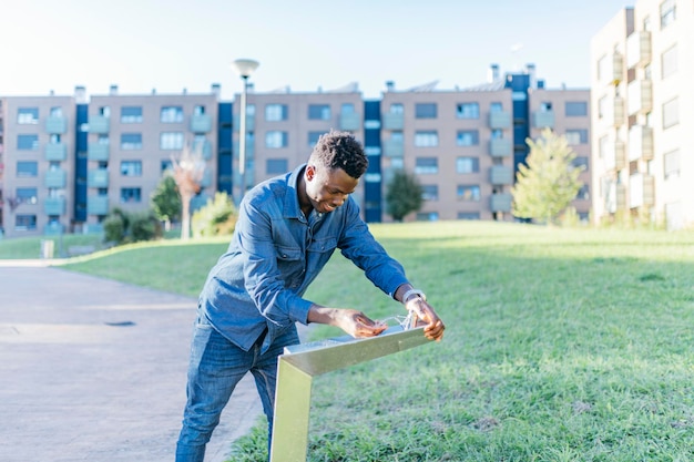 Joven afroamericano usando una fuente de agua en el parque en un día soleado