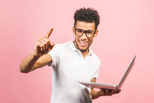 Joven afroamericano usando laptop sobre fondo rosa aislado