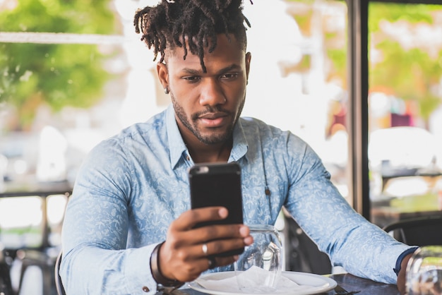 Joven afroamericano usando su teléfono móvil mientras está sentado en un restaurante.