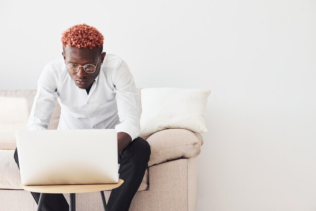 Joven afroamericano vestido con ropa formal sentado en el interior con una laptop en las manos