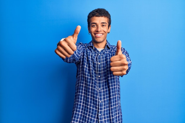 Joven afroamericano vestido con ropa informal aprobando hacer un gesto positivo con la mano, pulgares arriba sonriendo y feliz por el éxito. gesto ganador.