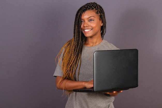 Joven afrobrasileña sosteniendo un cuaderno trabajando con una computadora portátil