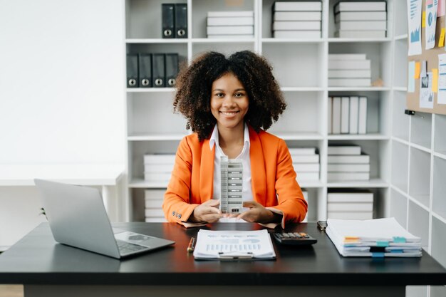 Foto un joven agente inmobiliario trabaja con una computadora portátil y una tableta en una mesa en una oficina moderna y una casa pequeña a su lado