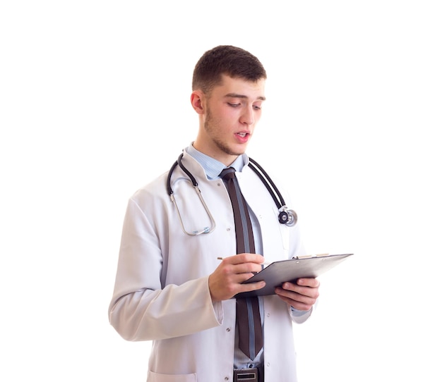 Joven agradable con camisa azul, corbata y bata de médico con estetoscopio en el cuello sosteniendo una carpeta