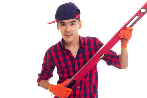 Joven agradable con camisa a cuadros roja con guantes naranjas y gorra azul con nivel rojo