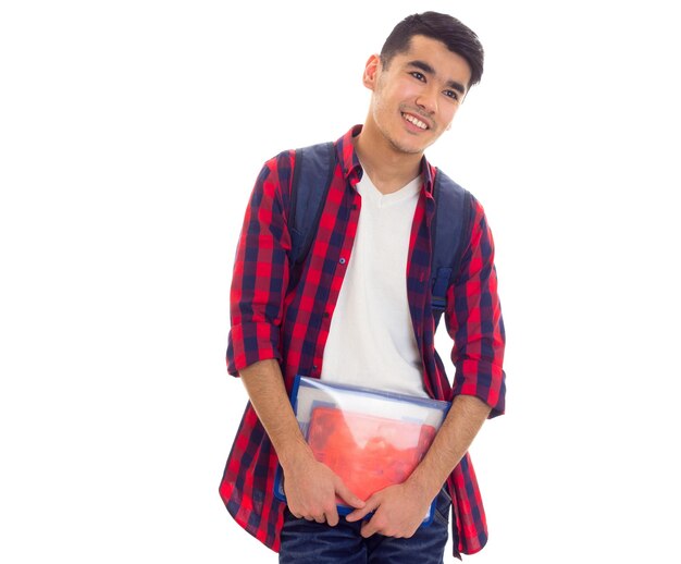 Un joven agradable con camisa a cuadros roja con mochila azul y carpeta con cuadernos