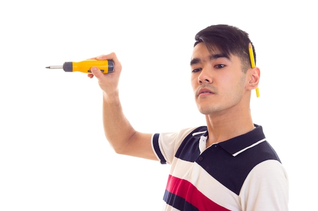 Un joven agradable con camiseta blanca y azul con un lápiz detrás de la oreja sosteniendo un destornillador amarillo