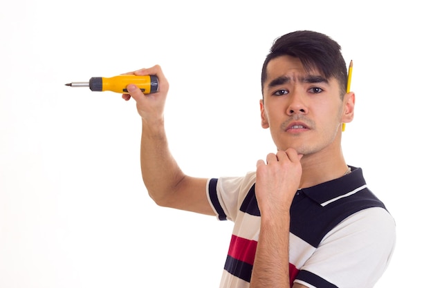 Un joven agradable con camiseta blanca y azul con un lápiz detrás de la oreja sosteniendo un destornillador amarillo