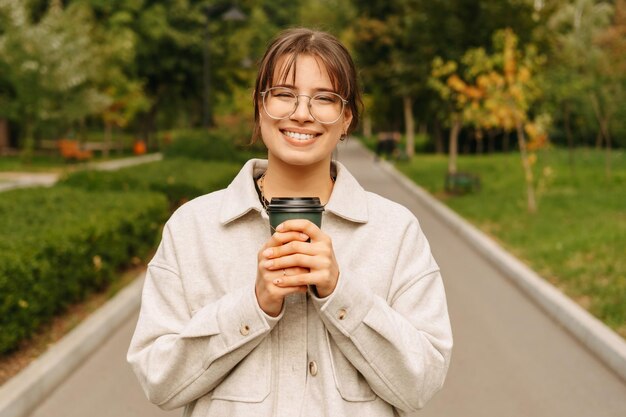 Una joven agradable disfrutando de su café para llevar mientras camina por el parque