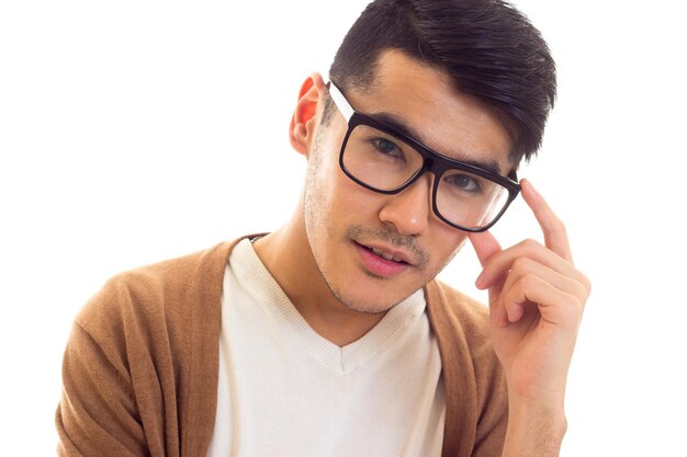 Joven agradable con el pelo negro en la chaqueta de punto marrón de camiseta blanca con gafas negras en el estudio