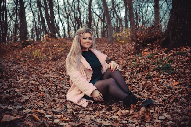 Una joven agradable con ropa informal y el pelo largo está sentada en el bosque de otoño