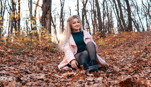 Una joven agradable con ropa informal y el pelo largo está sentada en el bosque de otoño