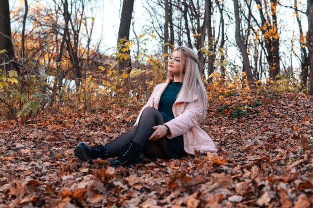 Una joven agradable con ropa informal y el pelo largo está sentada en el bosque de otoño