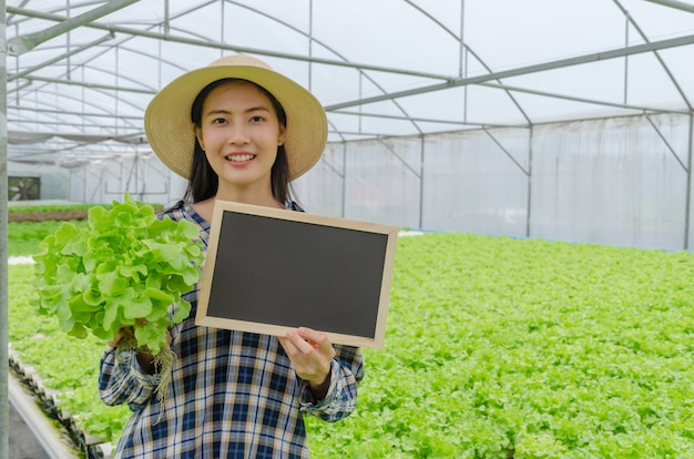 Joven agricultor amigable asiática mostrando pizarra en blanco y sosteniendo lechuga hidropónica fresca