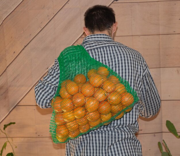 Un joven agricultor con una bolsa de naranjas en la espalda se beneficia del concepto de naranjas