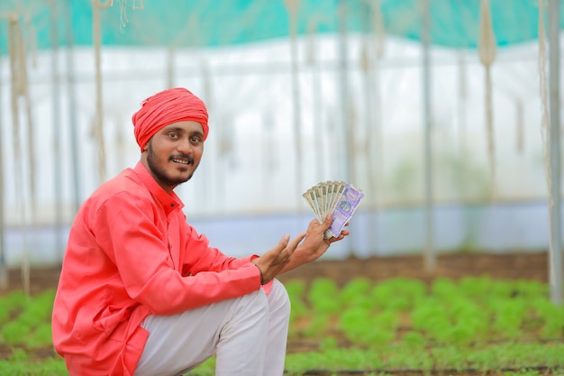 Joven agricultor indio contando y mostrando dinero en invernadero o polyhouse