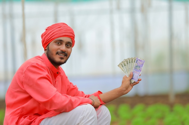 Joven agricultor indio contando y mostrando dinero en invernadero o polyhouse