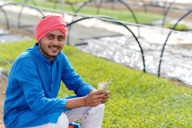 Joven agricultor indio contando y mostrando dinero en invernadero