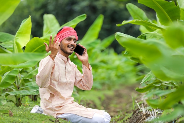 Joven agricultor indio hablando por teléfono inteligente en el campo de la agricultura bananera.