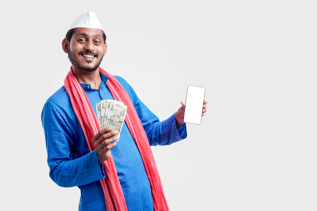 Joven agricultor indio mostrando smartphone y dinero sobre fondo blanco.