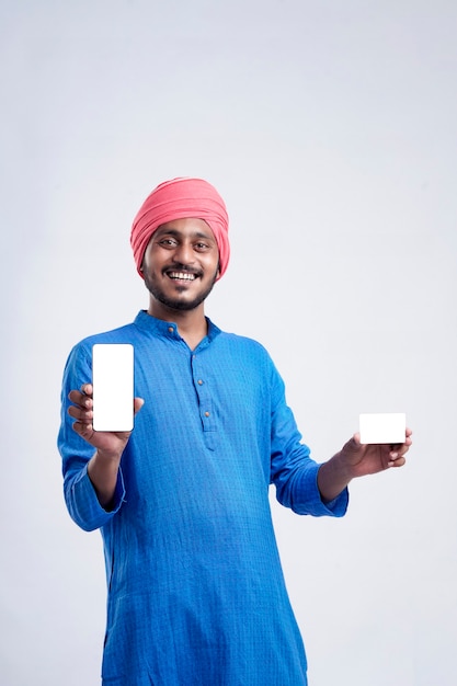 Joven agricultor indio mostrando tarjeta y smartphone sobre fondo blanco.