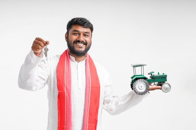 Joven agricultor indio mostrando tractor de juguete sobre fondo blanco.