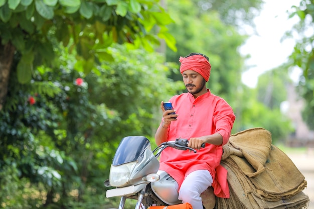 Joven agricultor indio en moto y usando teléfonos inteligentes.