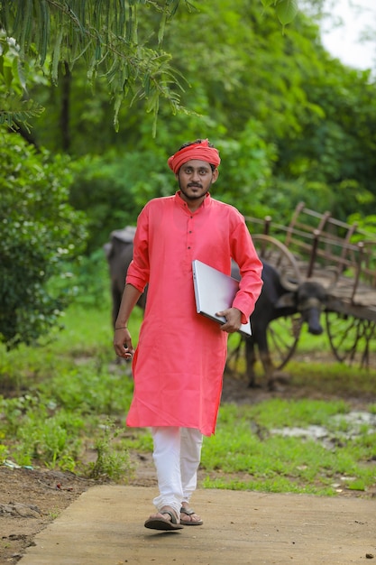 Joven agricultor indio con portátil en el campo