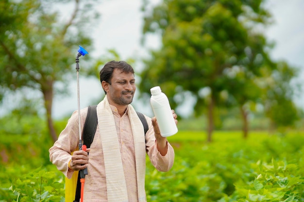 Joven agricultor indio que muestra la botella de fertilizante líquido en el campo de la agricultura.