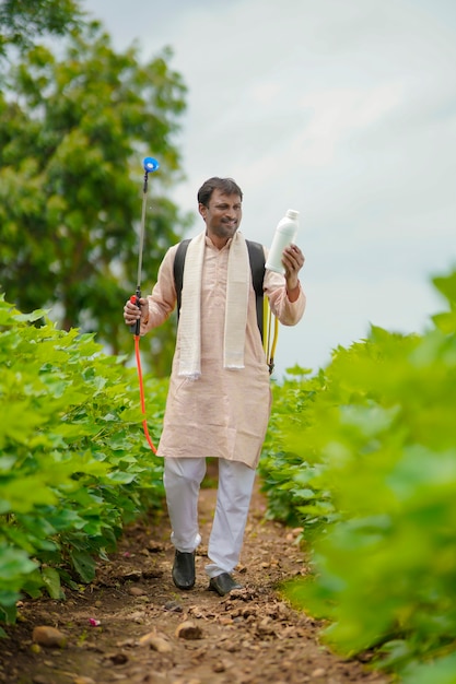 Joven agricultor indio que muestra la botella de fertilizante líquido en el campo de la agricultura.